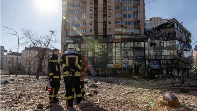 رجال الإطفاء يقفون وسط أنقاض مبنى سكني أصيب بصاروخ في 26 فبراير/ شباط 2022 في كييف، أوكرانيا.