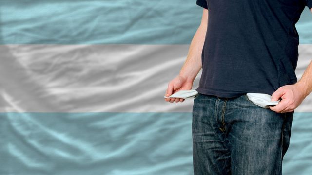 Un hombre muestra sus bolsillos vacíos frente a una bandera de Argentina