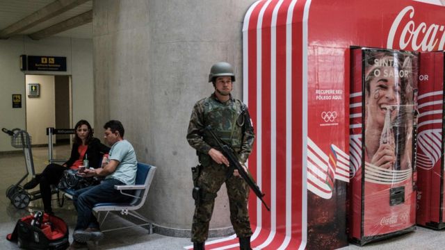 Un soldado en guardia al lado de una publicidad de Coca Cola