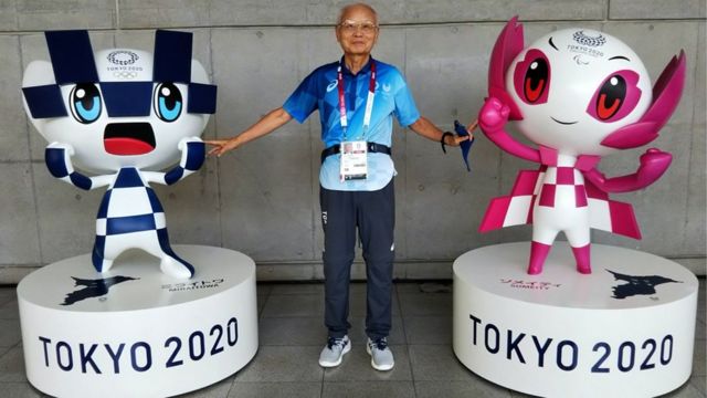 Katsuya Kato, a 79-year-old volunteer, posing between two Olympics mascots.