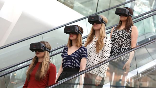 Mujeres en escaleras mecánicas con cascos de realidad virtual.