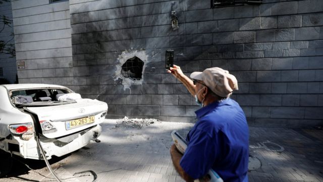 Un Israélien prend une photo avec son téléphone portable d'un immeuble résidentiel touché par une roquette lancée depuis Gaza, à Ashkelon, en Israël (14 mai 2021)