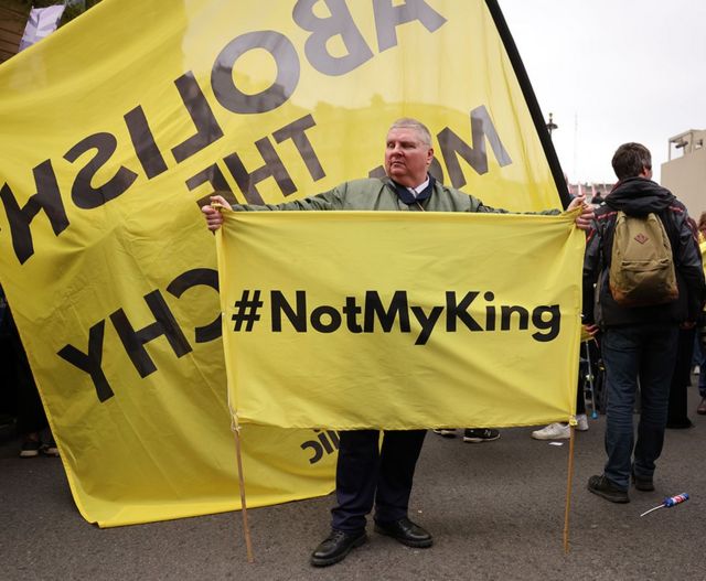 A man carries a banner with the hashtag #NotMyKing as anti-monarchy group Republic protest on the day of the Coronation