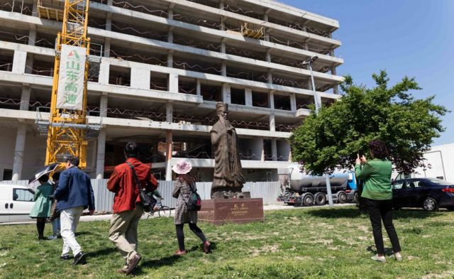 Chinese tourists walk past a Confucius statute outside the former Chinese embassy site