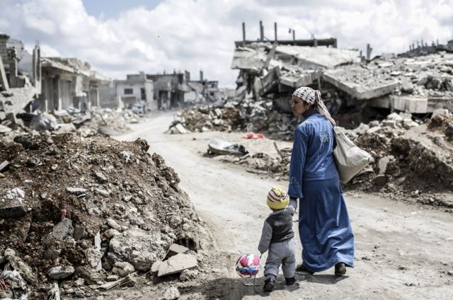 Mujer kurda pasea con un niño de la mano entre ruinas de Kobane.