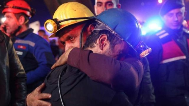 Dois mineiros se abraçam em foto noturna