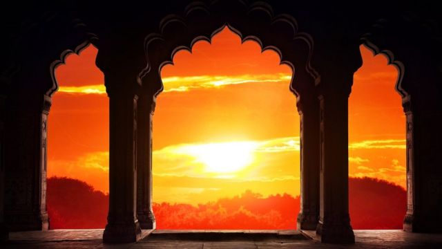 Indian arch silhouette in old temple at dramatic orange sunset sky background.
