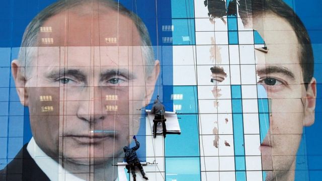 A poster of Vladimir Putin and Dmitry Medvedev being attached to an office building in 2011