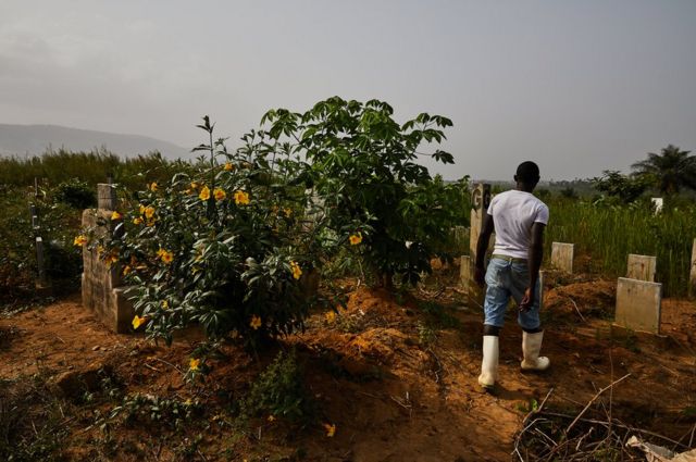 A graveyard worker with his back to the camera walks through Waterloo Ebola Graveyard. Sierra Leone.