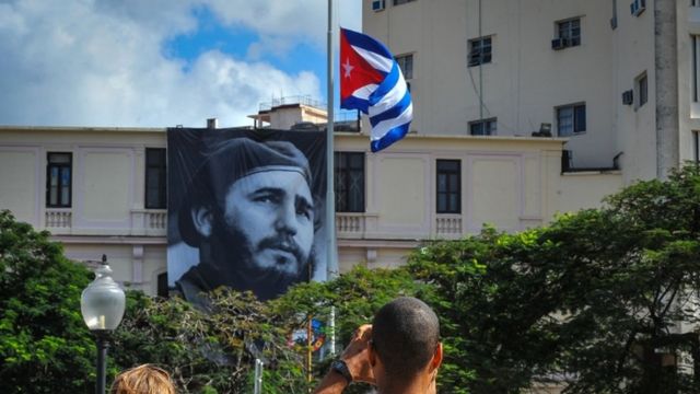 झुके राष्ट्रीय ध्वज को देखते क्यूबा के नागरिक
