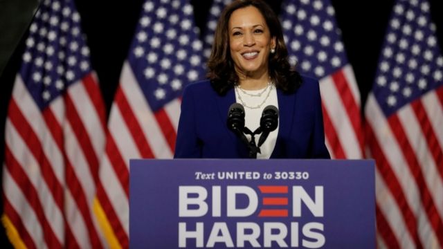 Kamala Harris standing in front of American flags at event in Wilmington, Delaware