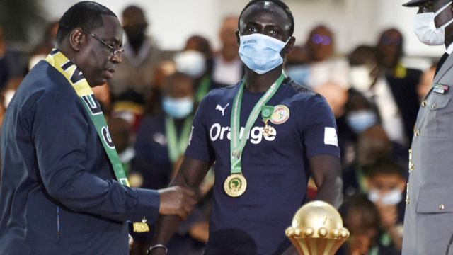 Senegal's President Macky Sall (L) decorates Senegal's forward Sadio Mane (C) during the decoration ceremony near the Palace of the Republic in Dakar on 8 February 2022