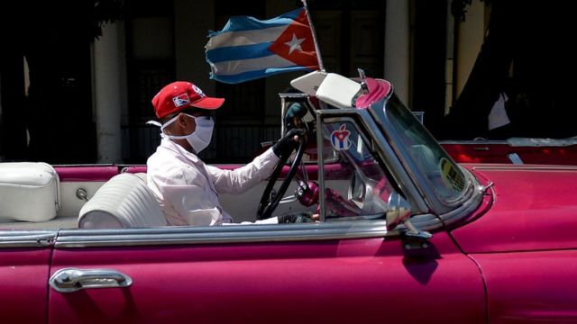 Un hombre con mascarilla manejando un auto antiguo en Cuba