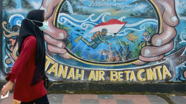 Warga mengenakan masker saat berjalan di dekat sebuah mural di Kota Ambon, Maluku, Rabu (7/7/2021).