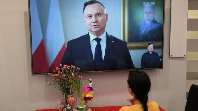 Uma mulher vê o discurso discurso do presidente da Polônia na televisão