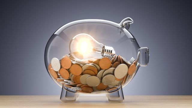 Cofre em forma de porquinho transparente, com moedas e uma lâmpada dentro