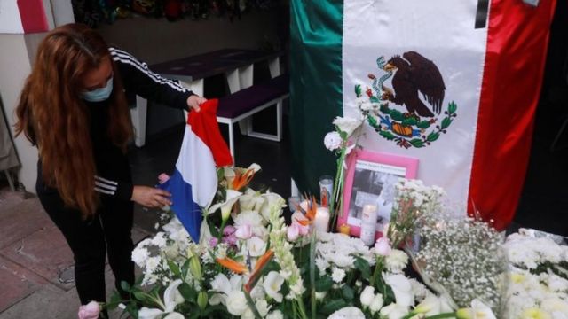 A woman holds the French flag next to the Mexican flag and some flowers