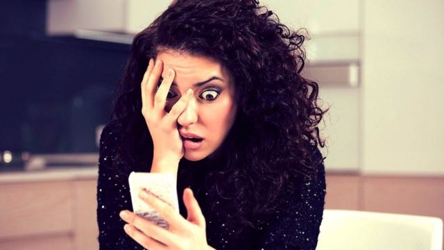 Mujer mirando un teléfono celular con actitud angustiada.