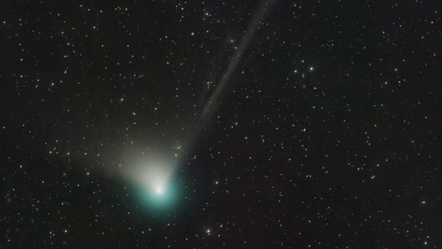 A green comet leaves its trail in a starry sky
