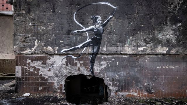 Mural de uma ginasta com um colar cervical acenando uma fita é visto na parede de um prédio destruído em Irpin
