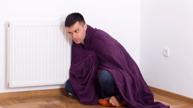 Man sitting by radiator in blanket