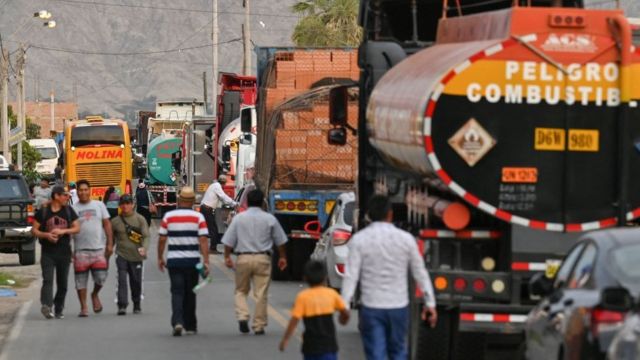 Personas camina junto a un grupo de camiones parado en una carretera peruana.