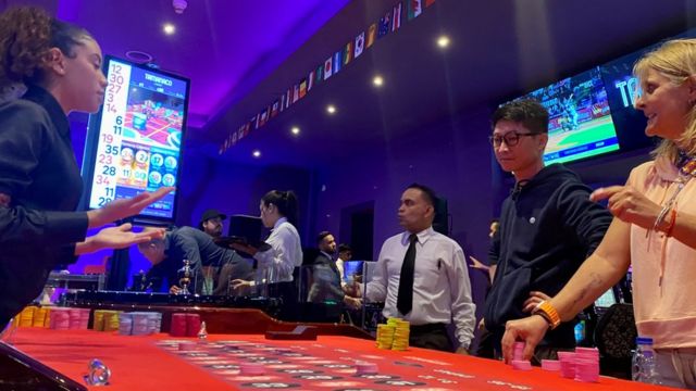 Fotografia colorida mostra pessoas em uma mesa de apostas
