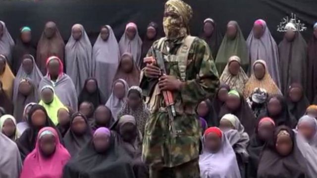 A still from a Boko Haram video showing a militant in front of some of the Chibok girls