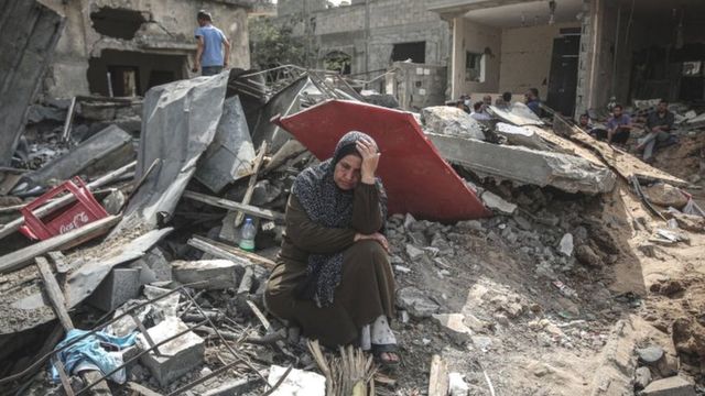 A Palestinian woman reacts as she stands on the debris of her destroyed house