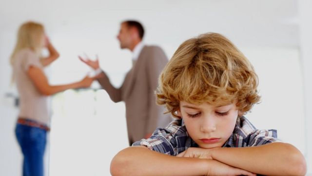 A sad boy hears an argument from his parents in the background