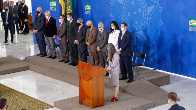 Foto com ângulo amplo mostra Bolsonaro e vários participantes do evento em pé e com cabeça baixa