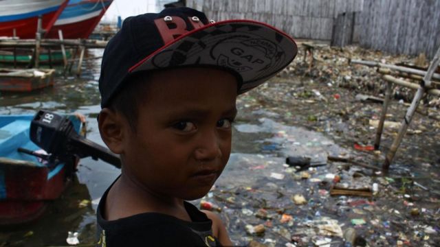 Niño frente a un basural de plástico.