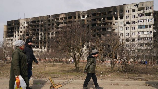 مدنيون يمرون بجانب مبنى دمره القصف الروسي بمدينة ماريوبول.