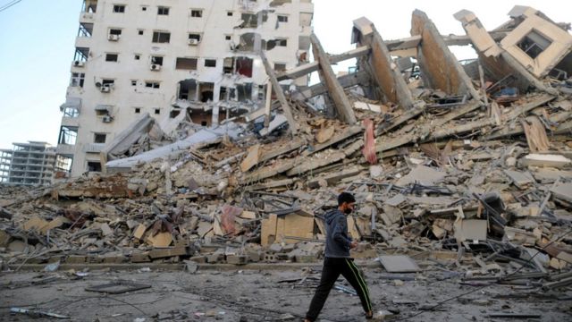 Un Palestinien passe devant une tour d'habitation détruite par une frappe aérienne israélienne dans la ville de Gaza (12 mai 2021)