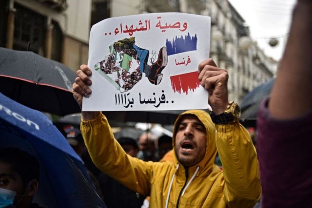 متظاهر يرفع لافتة مكتوب عليها "وصية الشهداء فرنسا برا"