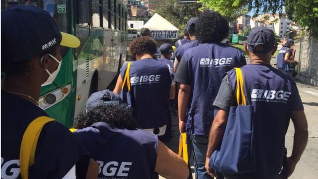 Recenseadores com coletes do IBGE de costas ao lado de um ônibus