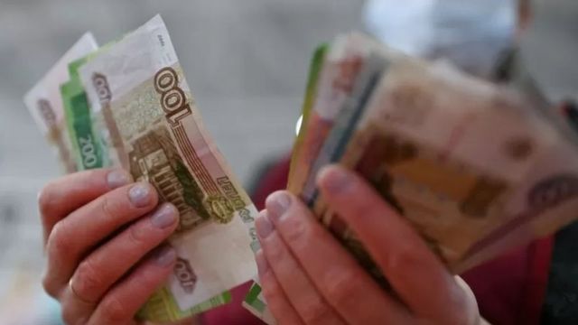 Pessoa segurando notas do rublo, o dinheiro russo