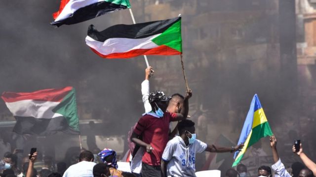 Sudanese demonstrators raise national flags as they take part in a protest in the city of Khartoum