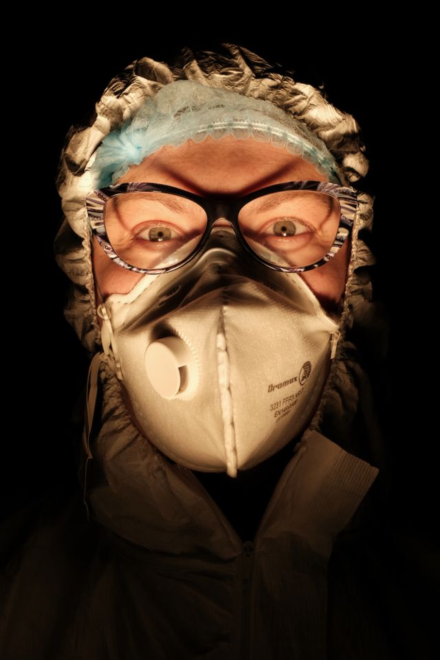 Seorang perawat mengenakan masker dengan latar belakang ruangan yang gelap