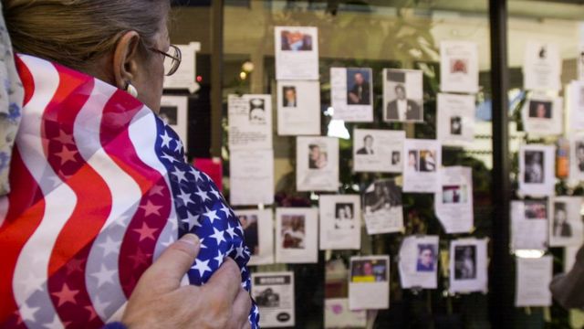 Una mujer envuelta en la bandera de Estados Unidos observa un mural con las víctimas del 11 S