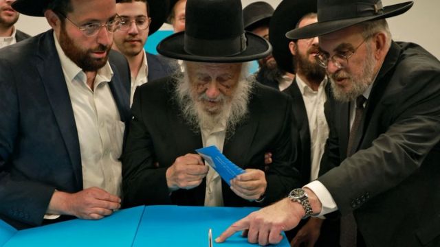 A group of Orthodox Jews help a community elder to vote in the parliamentary elections.