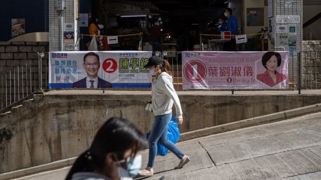 Pedestrians walk past posters for a candidates for the legislative elections in Hong Kong, China, 02 December 2021. The 2021 Hong Kong legislative general election will take place on 19 December 2021, over a year after being postponed and following a drastic Beijing-imposed electoral system overhaul.