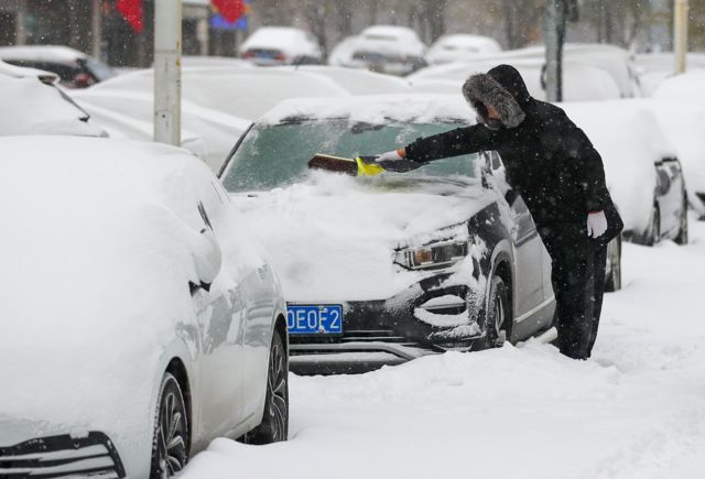 辽宁沈阳的市民清理车上的积雪。