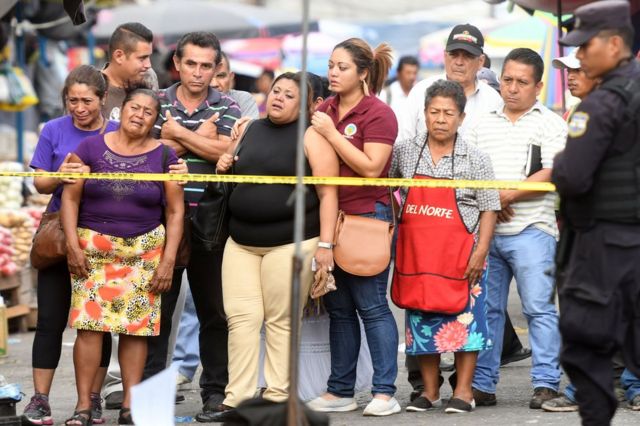 Una decena de salvadoreños tras el cordón policial colocado en una escena de crimen en San Salvador el 15 de marzo de 2017.