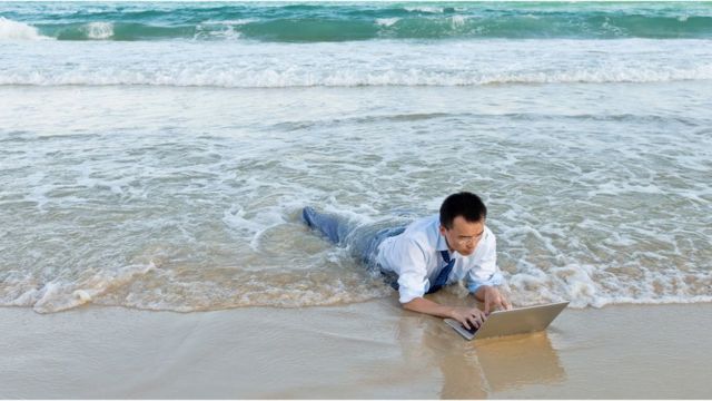 Chinese man lying near the waves with his suit and laptop