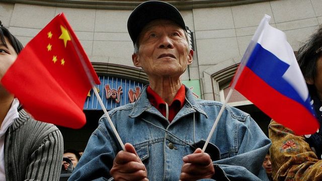 Un hombre sostiene la bandera china en una mano y la de Rusia en la otra