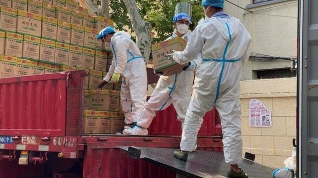 2022年4月21日，身穿防护服的人员从运往上海的卡车上卸下标有鲜味生抽的包装箱