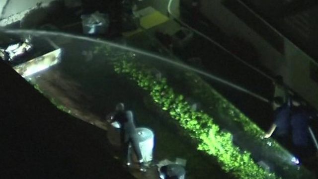 People spraying water on object outside of consulate and man closing rubbish bin