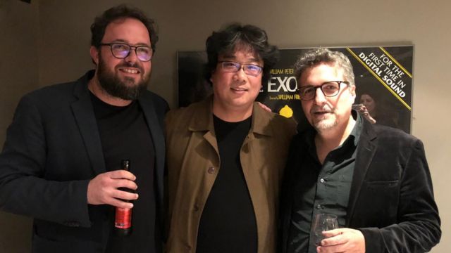 Juliano Dornelles, Bong Joon-ho e Kleber Mendonça posam para foto em corredor de cinema
