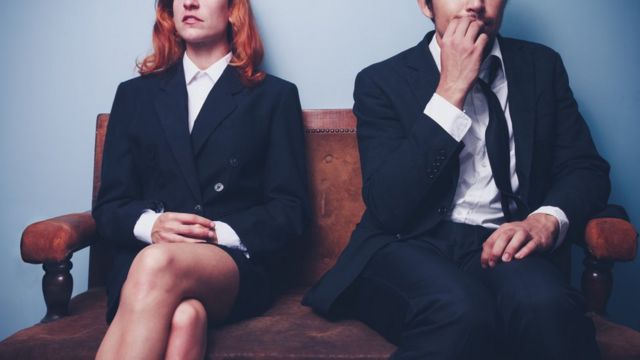 Mujer con las piernas cruzadas y hombre mordiéndose las uñas, en espera de una entrevista de trabajo.